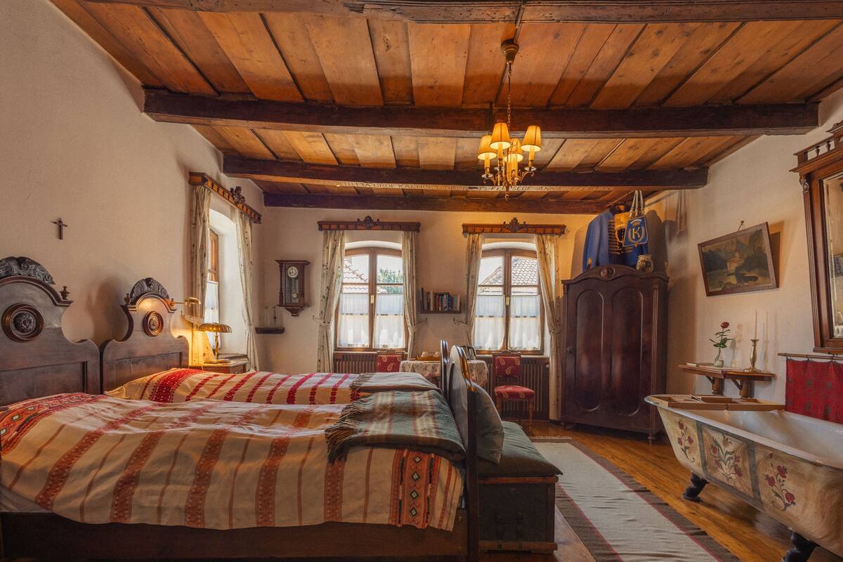 Une chambre traditionnelle avec un plafond en bois, un lit recouvert d’une literie à motifs, une baignoire de style ancien et un lustre.