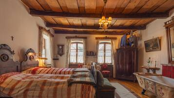 Una habitación tradicional con techo de madera, una cama con ropa de cama estampada, una bañera de estilo vintage y un candelabro.