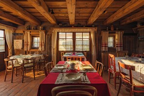A rustic wooden cabin with a dining area featuring wooden tables and chairs, a fireplace, and large windows with curtains. - Count Kalnoky's Transylvanian Guesthouse (Baraolt)