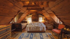 Un dormitorio en el ático con una cama grande, dos camas más pequeñas, un aparador, una silla y techo de madera.