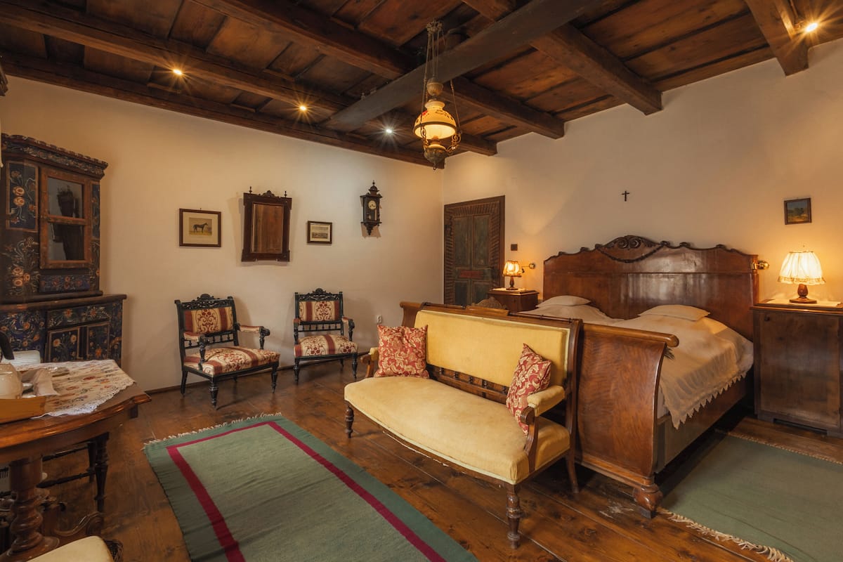 Une chambre traditionnelle avec un lit en bois, un canapé, une chaise, une armoire en bois et un luminaire suspendu.