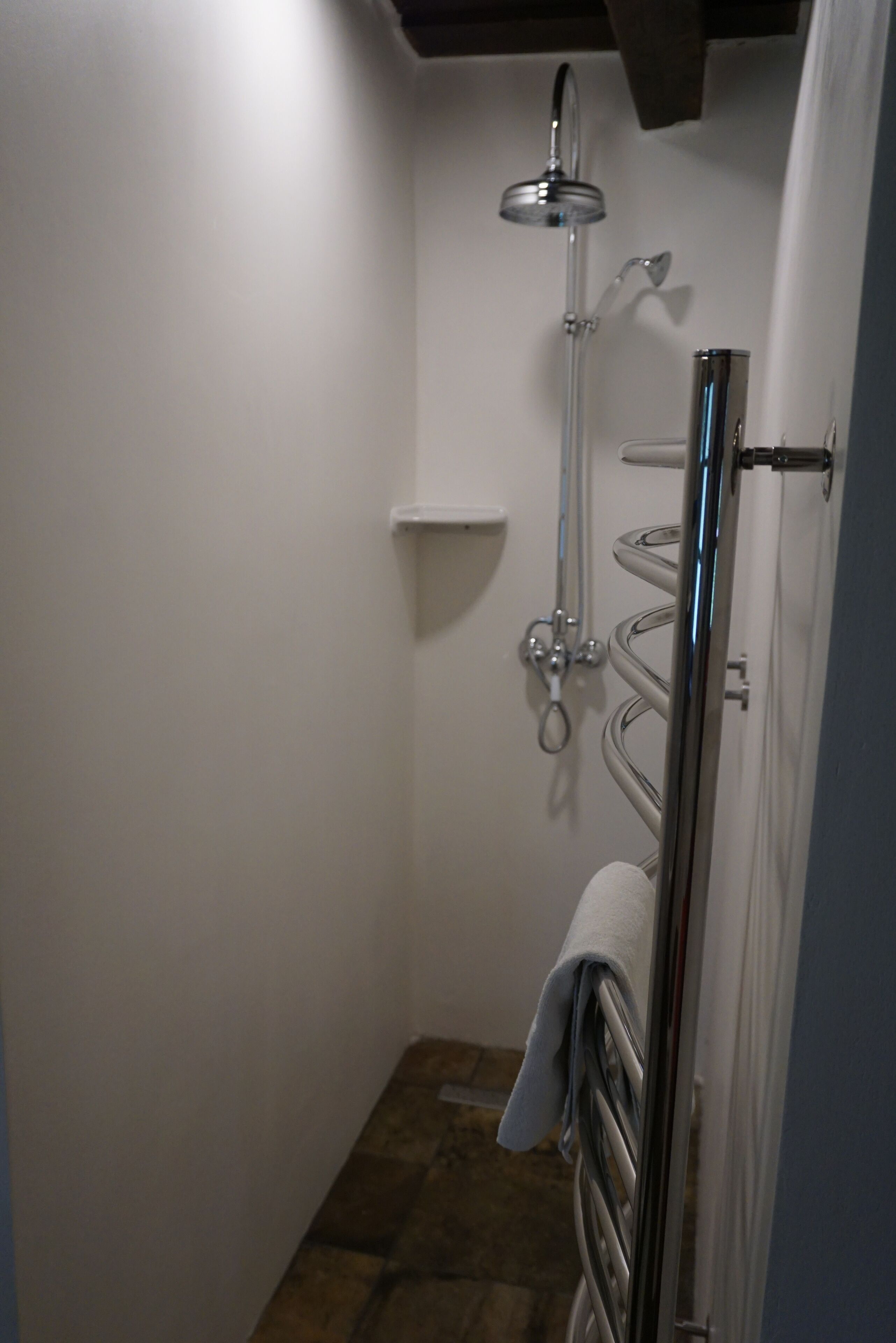 A small, narrow bathroom with a shower, a towel rack, and a shelf.