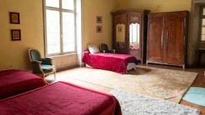 Una habitación con dos camas, una silla, un armario y un ventanal grande.