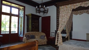 Una habitación con una cama de madera, un sofá, una silla y un amplio ventanal con cortinas.