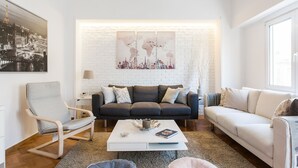 A modern living room with a white brick wall, a sofa, a chair, a coffee table, and a bookshelf. - Explore Athens with 2 Bedroom Condo (Athens)