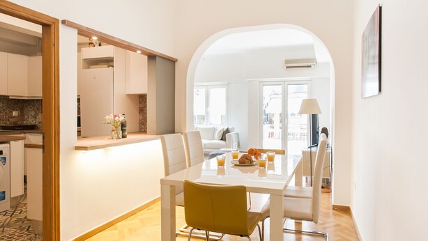 A modern kitchen with a wooden countertop, a dining area with a white table and chairs, and a view of the city through large windows. - Explore Athens with 2 Bedroom Condo (Athens)