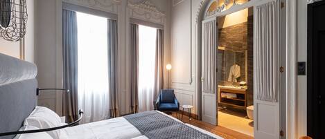 A hotel room with a large bed, a chair, and a bathroom visible through an open door.