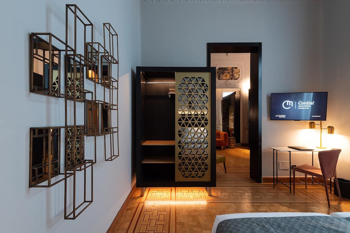 Une chambre d’hôtel comprenant un lit, un bureau avec une chaise, un téléviseur et un panneau décoratif mural.