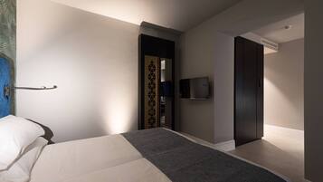 Una habitación de hotel moderna con una cama, un televisor de pantalla plana montado en la pared y una puerta de madera oscura.