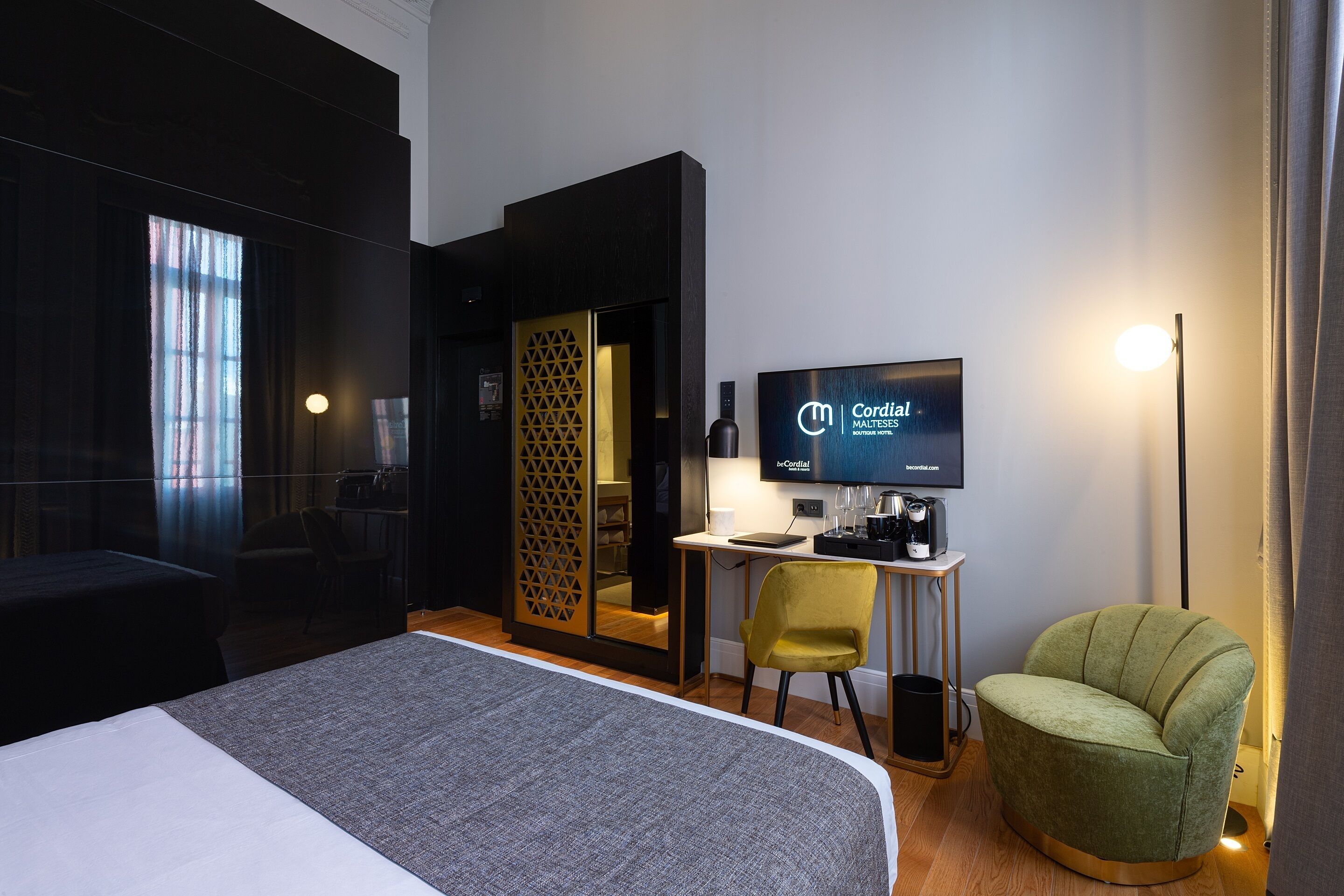 A hotel room with a bed, a desk with a computer, a chair, a television, and a lamp.