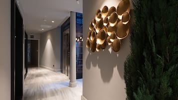 A hallway with a marble floor, a wall-mounted light fixture, and a green plant.
