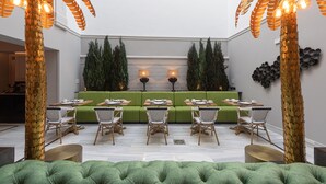 A modern dining area with green seating, wooden chairs, and decorative palm trees. - Boutique Hotel Cordial Malteses (Las Palmas de Gran Canaria)