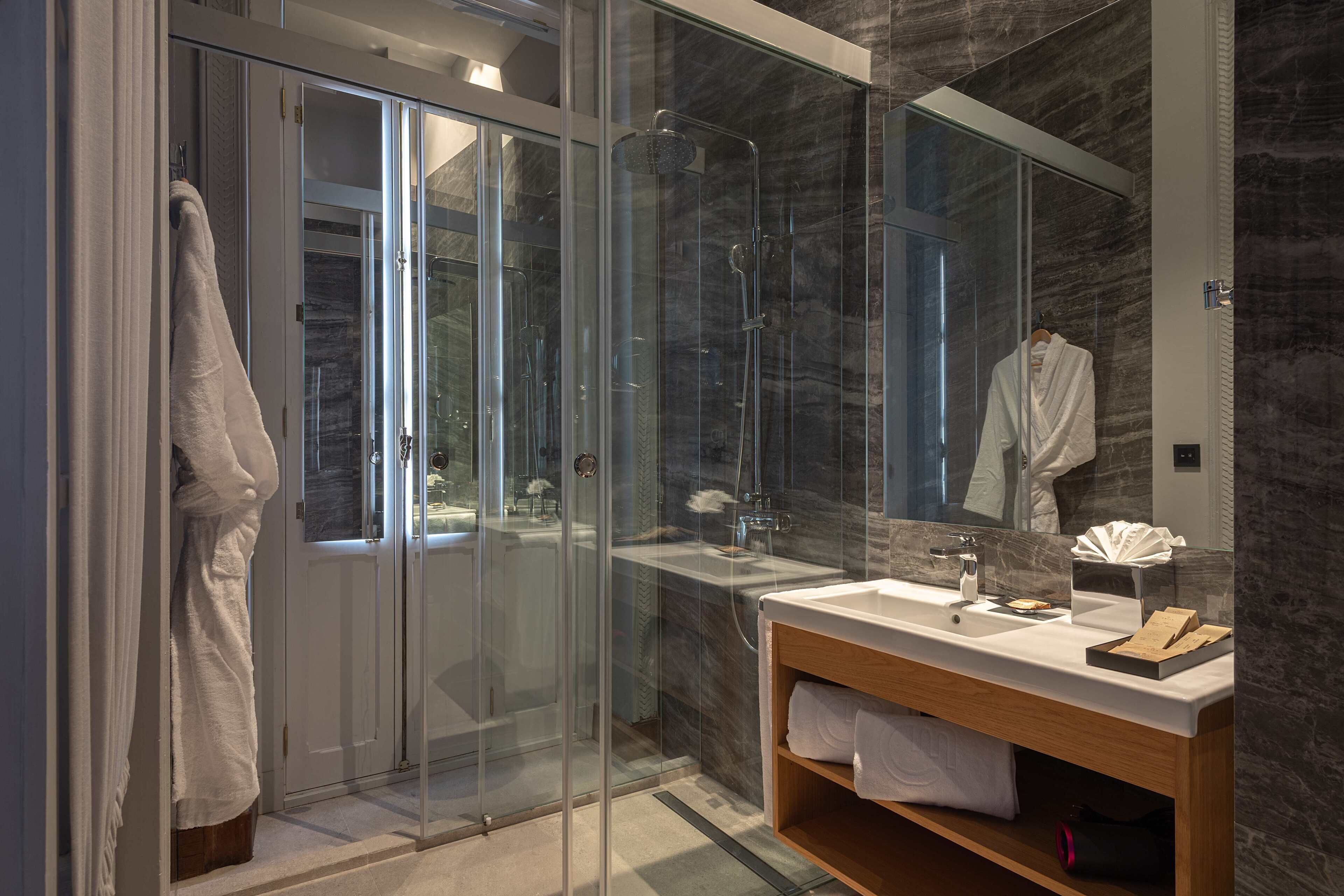 A modern bathroom with a glass-enclosed shower, a wooden vanity, and a marble backsplash.