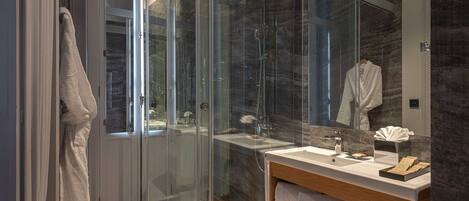 A modern bathroom with a glass-enclosed shower, a wooden vanity, and a marble backsplash.