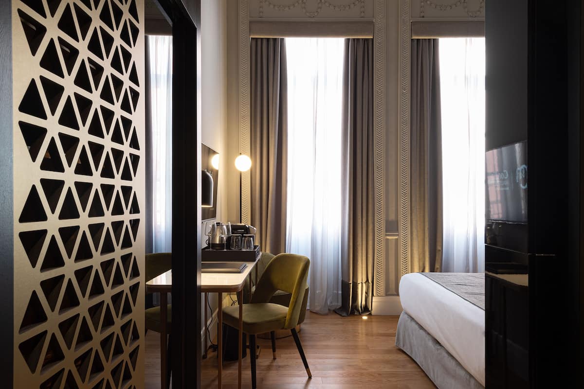 Une chambre d’hôtel comprenant un lit, un bureau avec une chaise, une télévision et un élément de séparation décoratif.