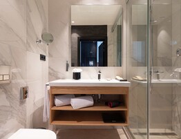 Un bagno moderno con parete in marmo, mobile vanità in legno, box doccia in vetro e uno specchio grande.