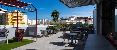 A rooftop terrace with outdoor seating, a pergola, and a view of the cityscape.