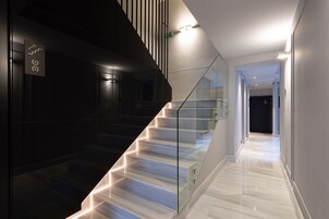 A modern staircase with glass railings and a lighted handrail, leading to a hallway with a polished floor and a door at the end.