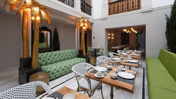 A spacious dining area with a long table set for a meal, surrounded by green sofas and wicker chairs. - Boutique Hotel Cordial Malteses (Las Palmas de Gran Canaria)