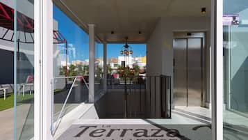 Una entrada a La Terrazas de Malta con un puerta de vidrio, una barandilla metálica y vista del paisaje urbano al fondo.
