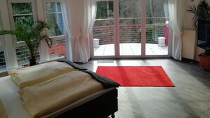 A bedroom with a bed, a red rug, and a balcony with a view of greenery. - Comfort apartment in the wildlife park (Koblenz)