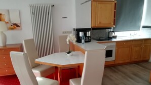 Une cuisine compacte avec un coin repas, comprenant une table blanche, des chaises et un petit îlot central avec une machine à café.