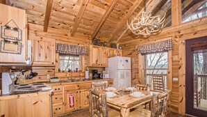 A wooden cabin kitchen with a dining table, chairs, and a refrigerator.