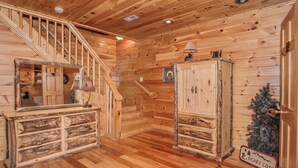A wooden interior with a staircase, a mirror, a cabinet, and a Christmas tree.
