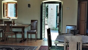 A dining area with wooden furniture, a clock on the wall, and a view through an open door. - Unique Stone House with the charm of past centuries (Herceg Novi)