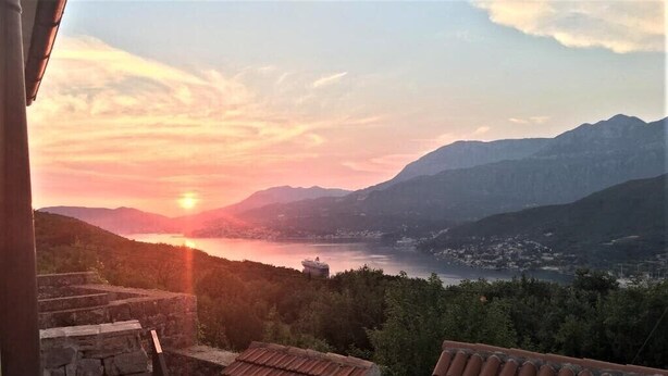 A view of a mountainous landscape with a sunset over a body of water, stone steps leading up to a building with a tiled roof. - Unique Stone House with the charm of past centuries (Herceg Novi)