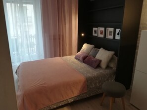 A bedroom with a bed, a bedside table, a chair, and a wall with framed pictures.