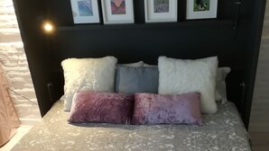 A bed with a patterned bedspread, multiple pillows, and framed pictures on the headboard. - YOUR PAUSE IN VALENCIA Center. July and August 10%. Discount (Valencia)