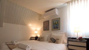 A neatly made bed with a rolled towel, a bedside lamp, and a nightstand with a lamp and a vase of flowers. - The Grich (Zagreb)