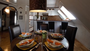 A dining area with a table set for four, a hanging lamp, and a view of the kitchen through an open archway. - The Grich (Zagreb)