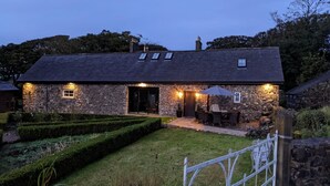 A stone house with a dark roof, a well-lit entrance, and a patio with outdoor seating. - Unique accommodation in the centre of Bushmills - dating back to 1745  (Bushmills)