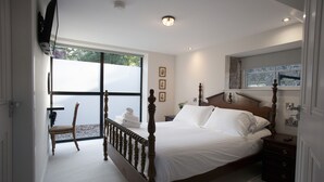 A bedroom with a large bed, a wooden headboard, a bedside table, a chair, a window, and a flat-screen TV mounted on the wall. - Unique accommodation in the centre of Bushmills - dating back to 1745  (Bushmills)