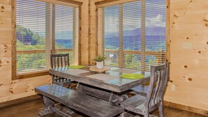 A wooden dining table with benches, large windows, and a view of the outdoors.