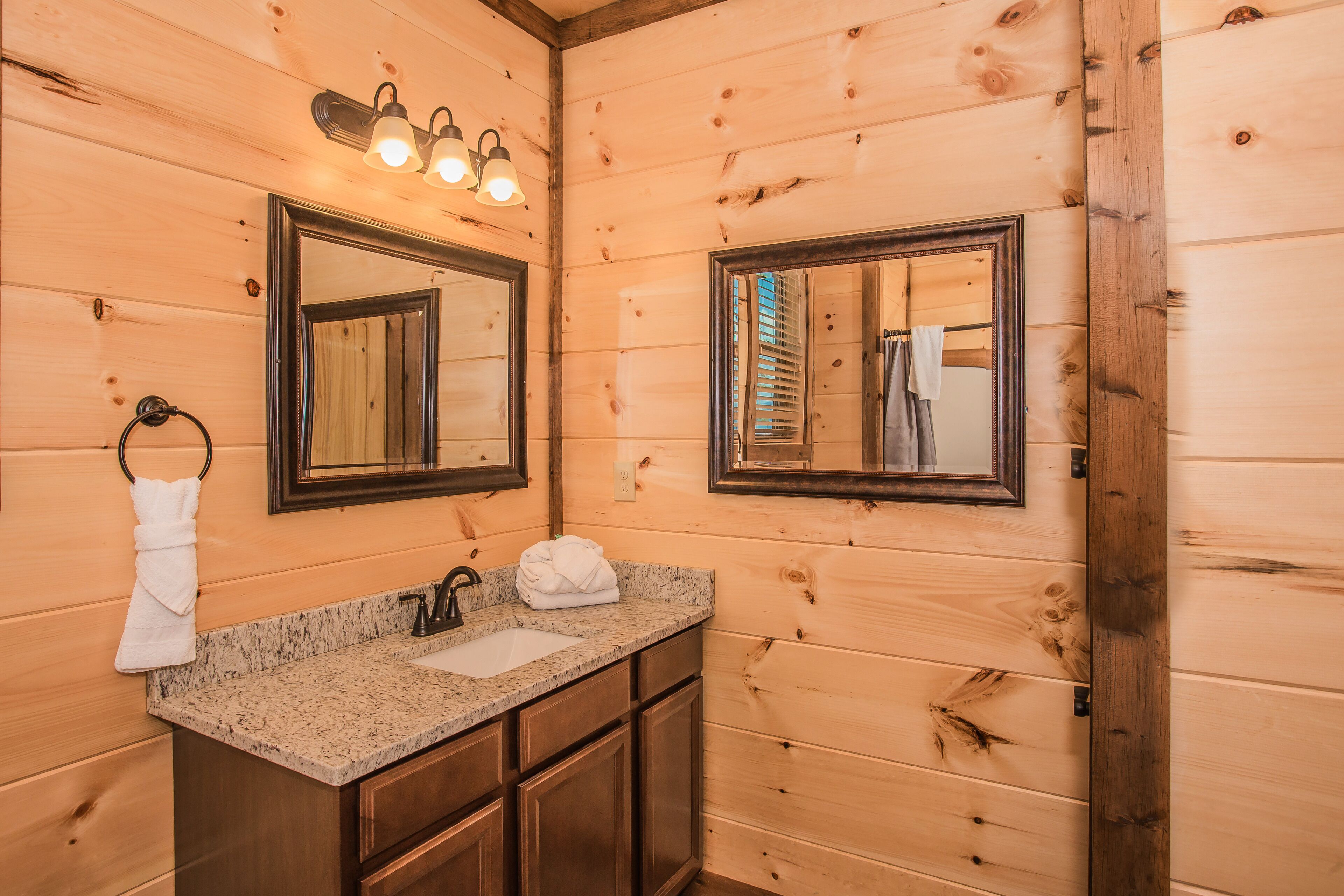 A wooden cabin bathroom with a granite countertop sink, two mirrors, and a towel rack.