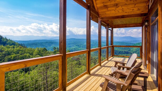 A wooden deck with Adirondack chairs overlooking a forested mountain range.