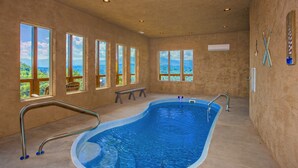 An indoor swimming pool with a view of mountains through large windows, a bench, and a metal pool ladder.