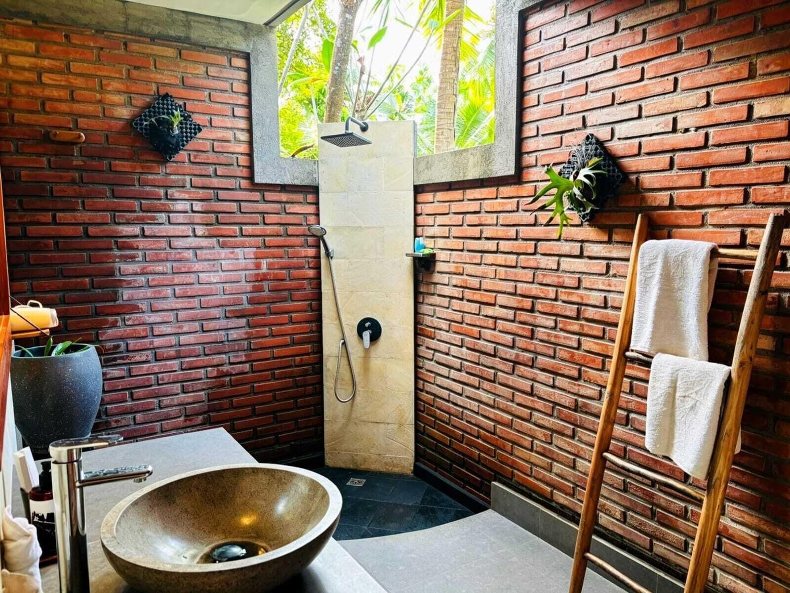 Un baño con pared de ladrillo, un lavabo grande, una ducha y una escalera de madera.