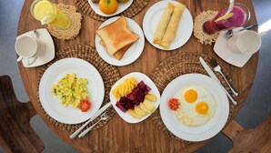 Een ronde houten tafel met ontbijtproducten, zoals toast, eieren, fruit en een smoothie.