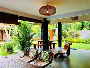 An outdoor patio with a wooden table, wicker chairs, and a hanging light fixture. - Coco Garden Pool Villas (Kubutambahan)
