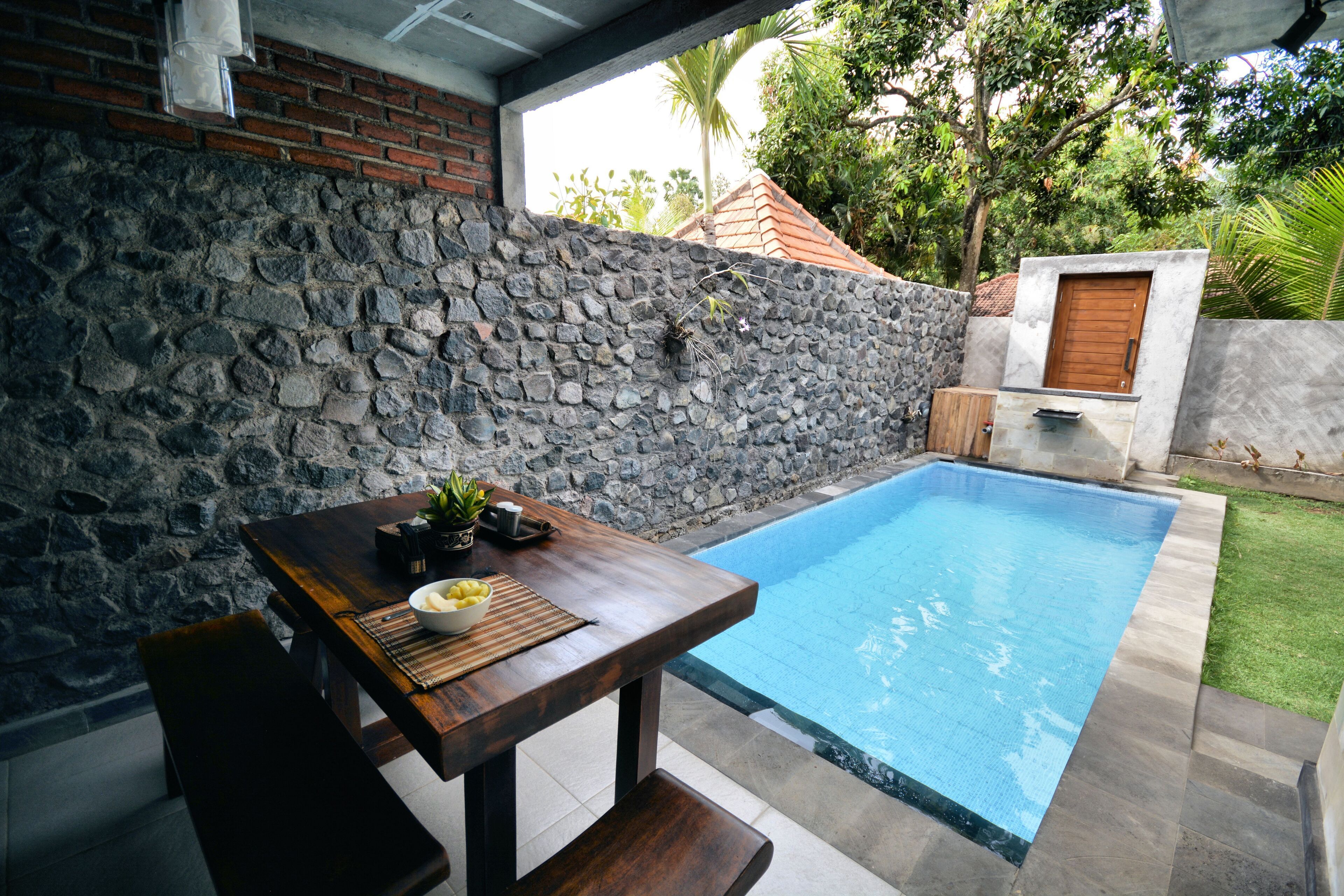 A stone wall, a wooden table with a bowl of lemons, and a swimming pool.
