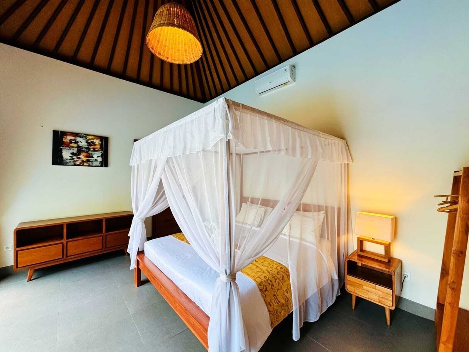 A bedroom with a canopy bed, bedside table, and a wall-mounted air conditioning unit.