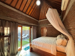A bedroom with a wooden ceiling, a canopy bed, and a view of an outdoor seating area. - Coco Garden Pool Villas (Kubutambahan)