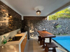 Uma cozinha moderna com uma parede de pedra, uma área de jantar com mesa e bancos de madeira, e uma piscina.