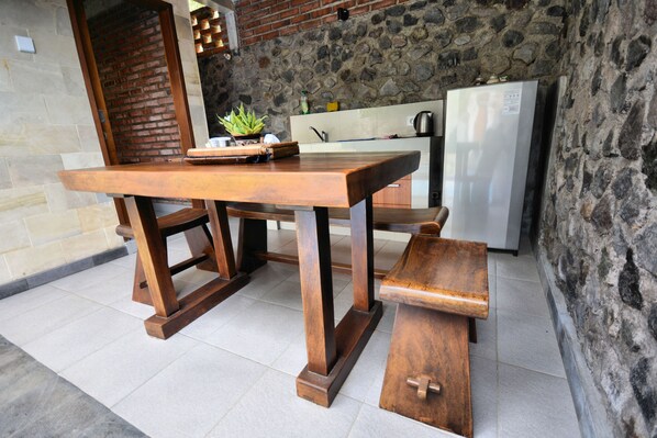 A wooden dining table with benches in a kitchen area with stone walls and a tiled floor. - Coco Garden Pool Villas (Kubutambahan)