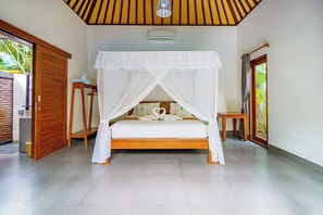 A bedroom with a four-poster bed, a bedside table, a wall-mounted air conditioning unit, and a wooden door. - Coco Garden Pool Villas (Kubutambahan)