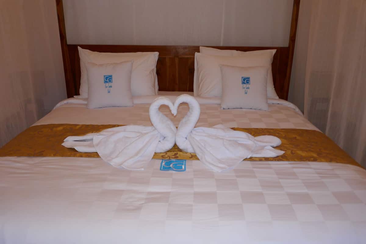 Quarto de hotel com uma cama, apresentando arranjo de toalhas em formato de coração e almofadas combinando.